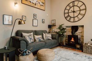 Bright and airy living room inside The Dovecote cottage at The Roost, featuring high open ceilings, a lit woodburner fireplace, and large French windows.