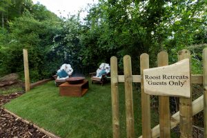 A private, remote Meadow Garden at The Roost Retreats with a fire pit, open-fire cooking setup, and outdoor seating surrounded by trees.